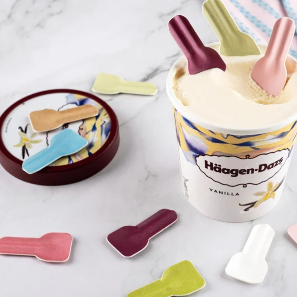 Cucharas de degustación de papel biodegradables en varios colores insertadas en helado de vainilla.