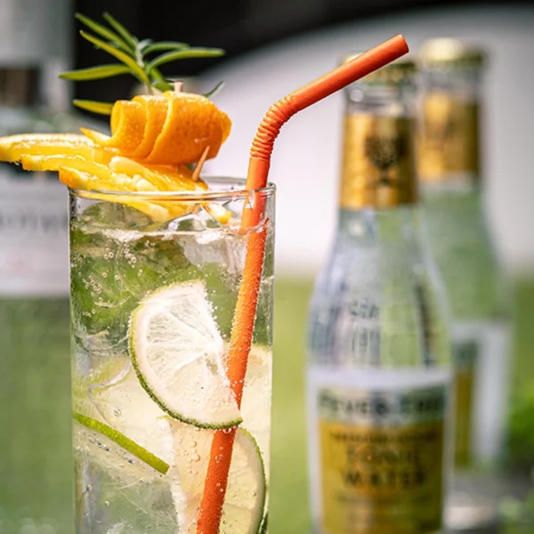 Pajita de papel naranja flexible en vaso de ginebra con tónica con lima y naranja. Pajita ecológica y compostable.