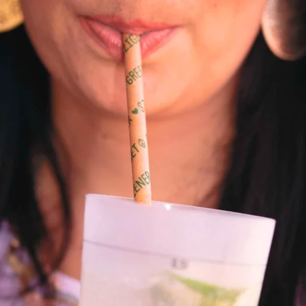 Persona bebiendo con pajita de papel ecológica y biodegradable en un vaso. Ideal para hostelería sostenible.