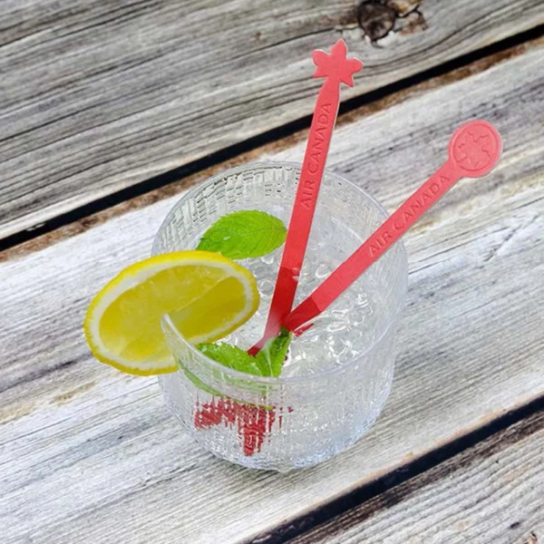 Dos removedores de bebidas de papel rojos "Aire Canadá" en vaso con hielo, limón y menta. Agitadores ecológicos biodegradables.