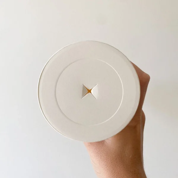 Tapa de papel compostable para vaso descartable, color beige, con orificio en cruz para pajita. Solución ecológica y sostenible.