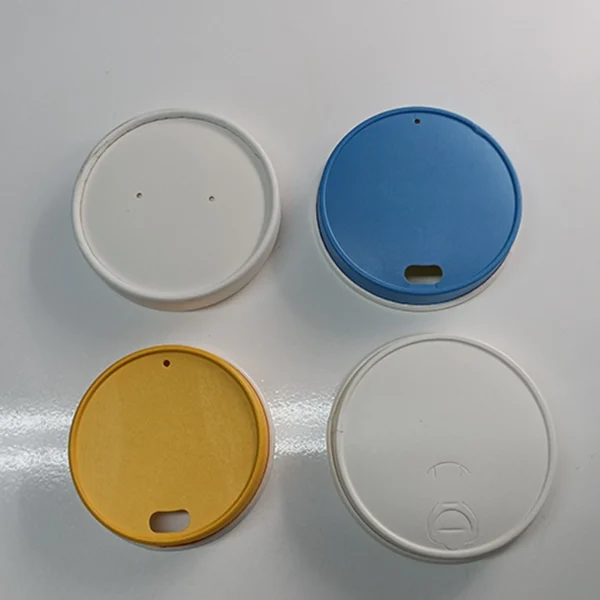 Cuatro tapas biodegradables para vasos de papel en colores blanco, azul y amarillo, ideales para café y bebidas para llevar.
