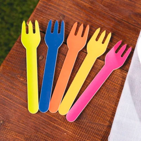Cinco tenedores descartables de papel en colores amarillo, azul, naranja, amarillo claro y fucsia sobre mesa de madera. Cubiertos ecológicos.